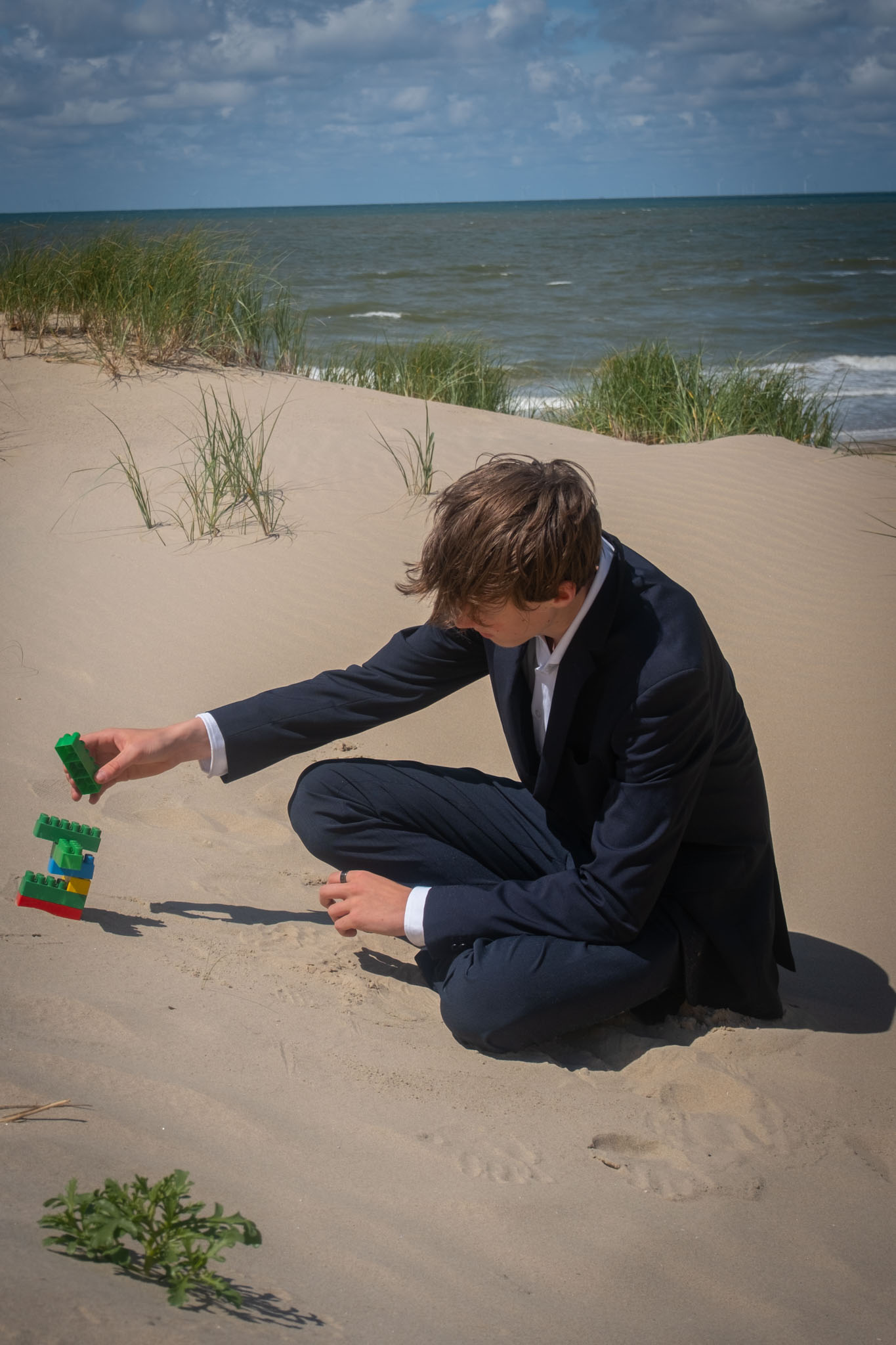 Een man in een pak zit met gekleurde bouwstenen op het strand