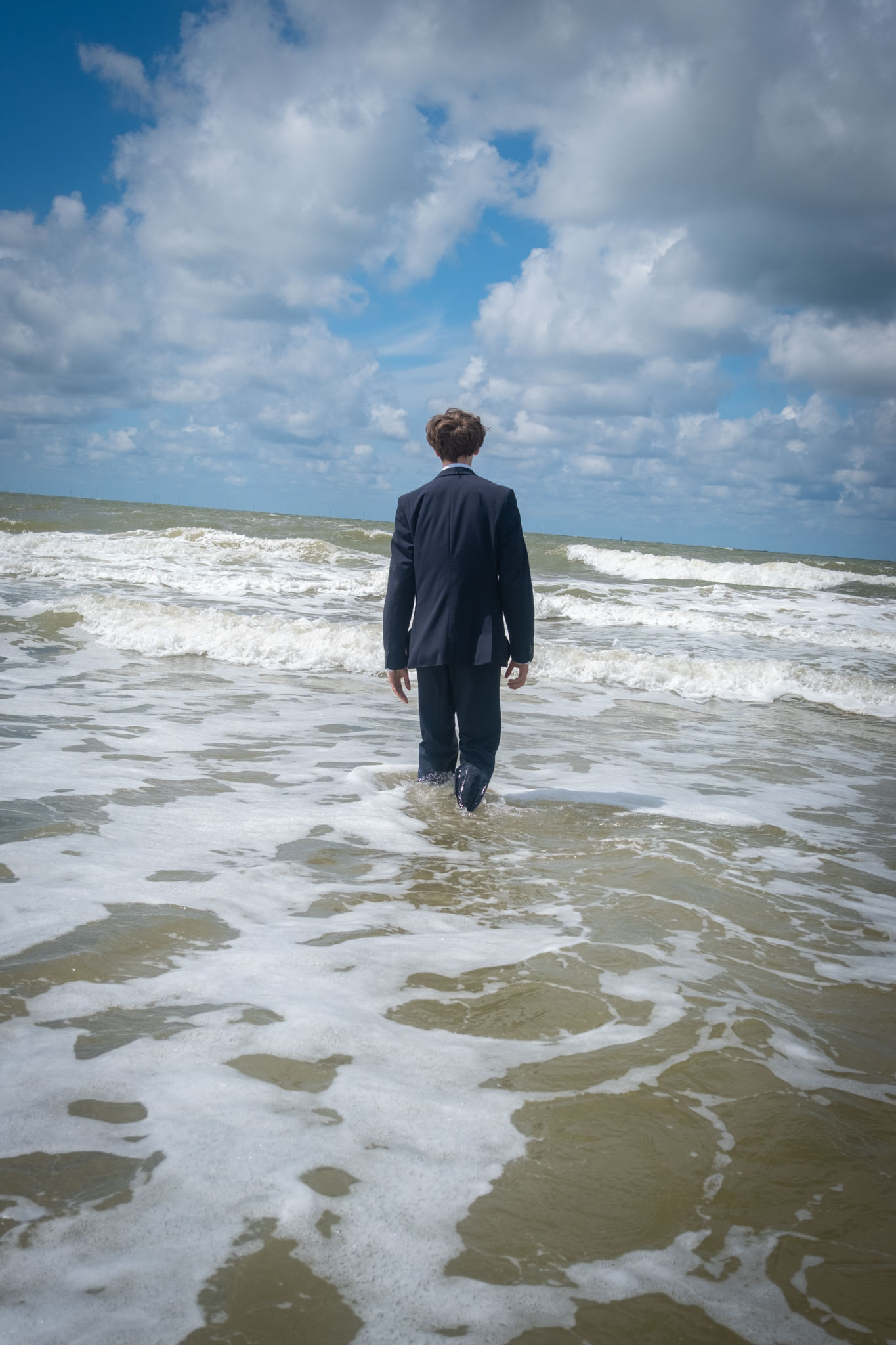 Een man in een donker pak loopt de zee in