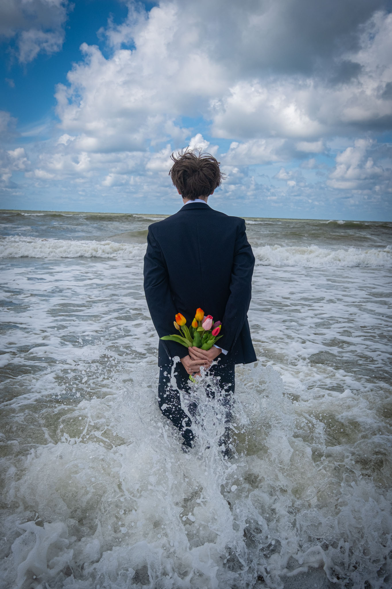 Een man staat met bloemen achter zijn rug in de branding