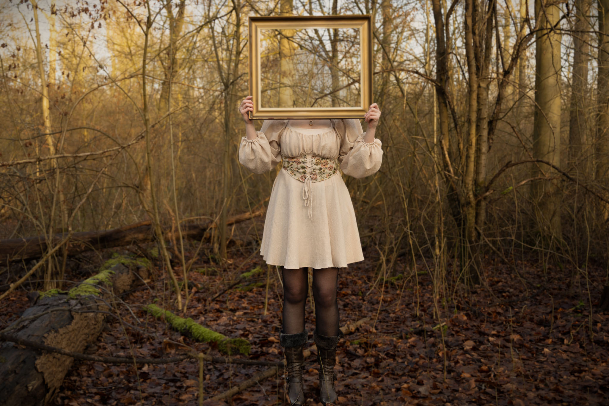 Een vrouw houdt een gouden lijst voor haar gezicht in het bos